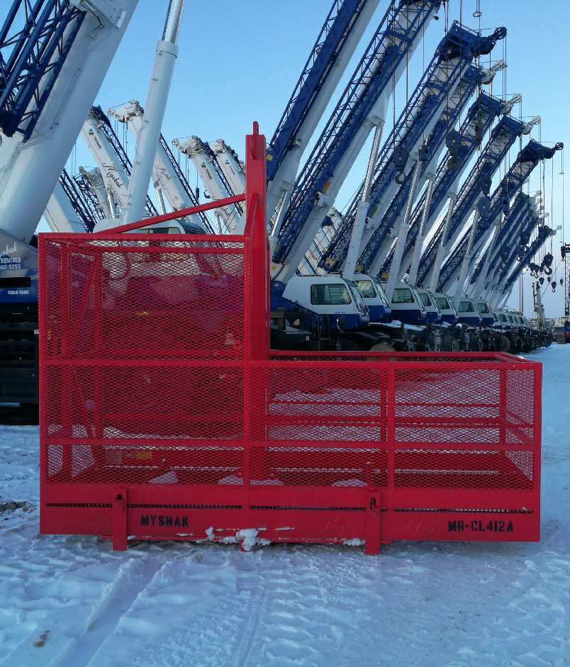 Forklift personnel cantilever basket on snow with cranes in background.