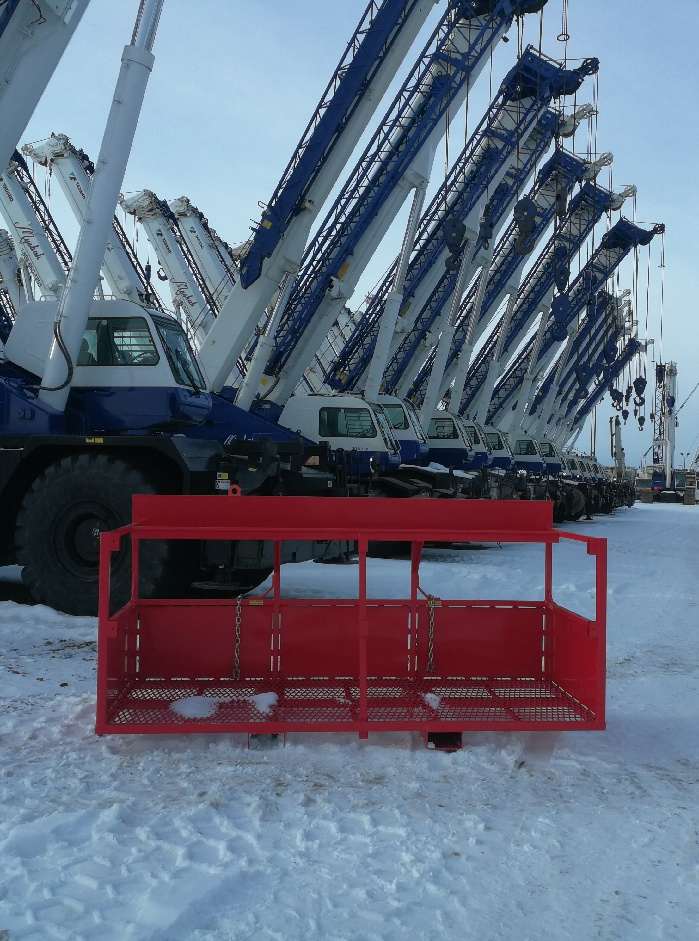 Material basket on side on snow with cranes in background.