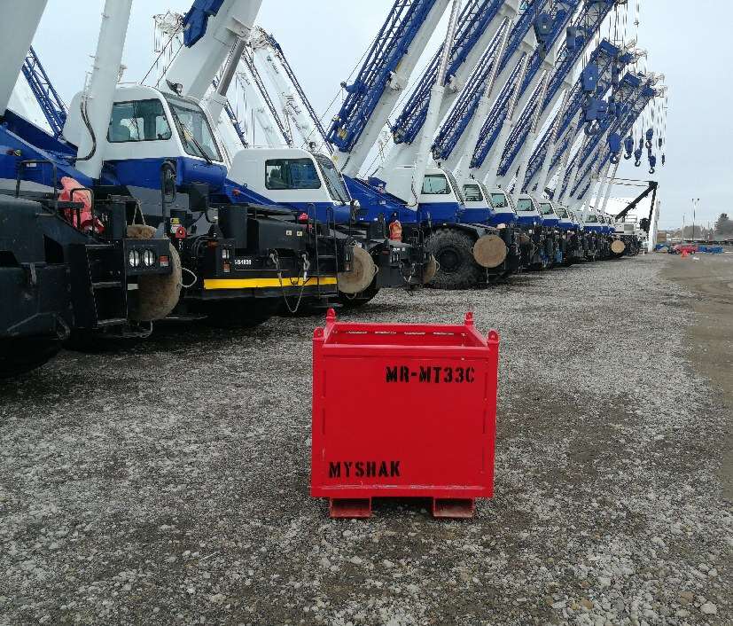 Small material basket on ground with cranes in background.