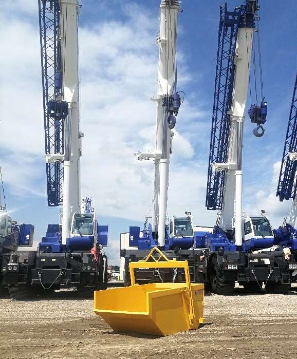 Yellow self dumping bin with cranes behind.