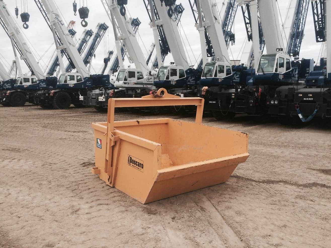 Yellow self dumping bin with cranes behind.